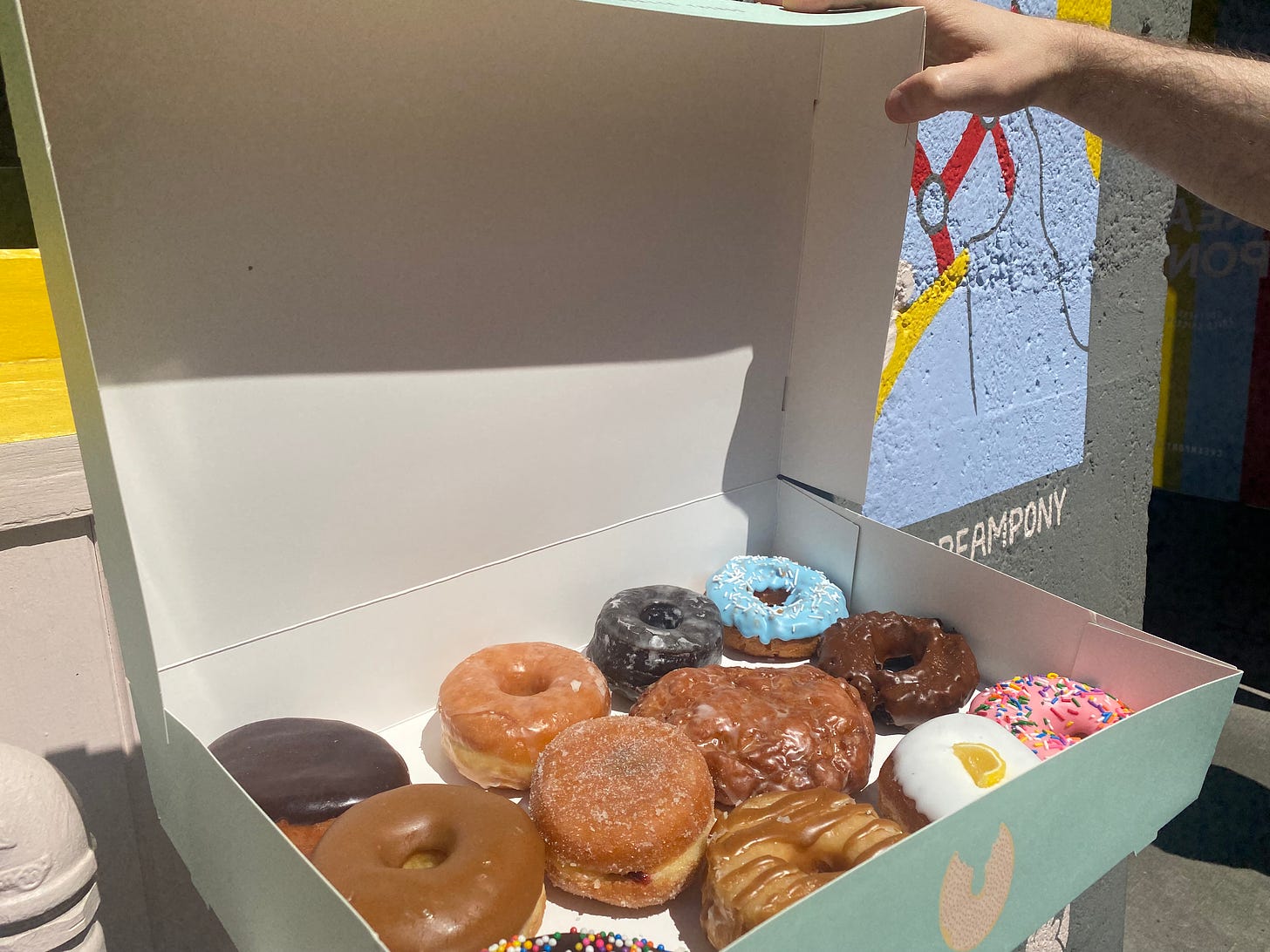 A baby blue box of a dozen donuts of different types, resting on a ledge outside of Cream Pony.