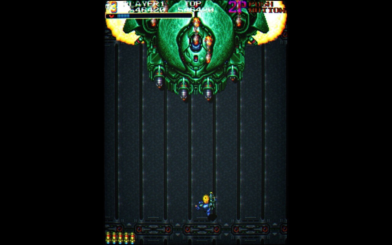 A screenshot of a boss from Out Zone, a huge tank-like ship with some mech characteristics, with four missile bays and destroyed cannons on the left and right. The "eye" in the center is its weak point, but only at specific moments in the fight.