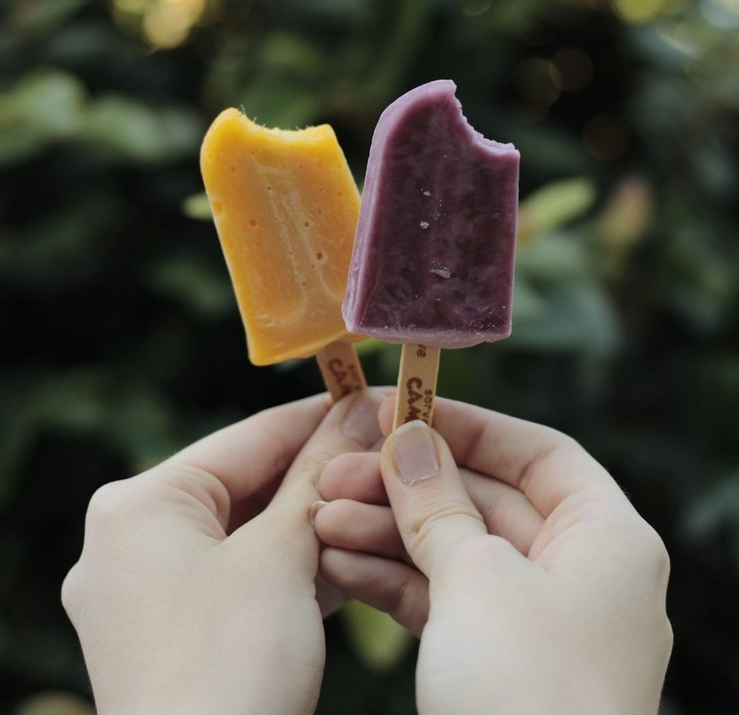 person holding yellow and pink ice cream person holding yellow and pink ice cream