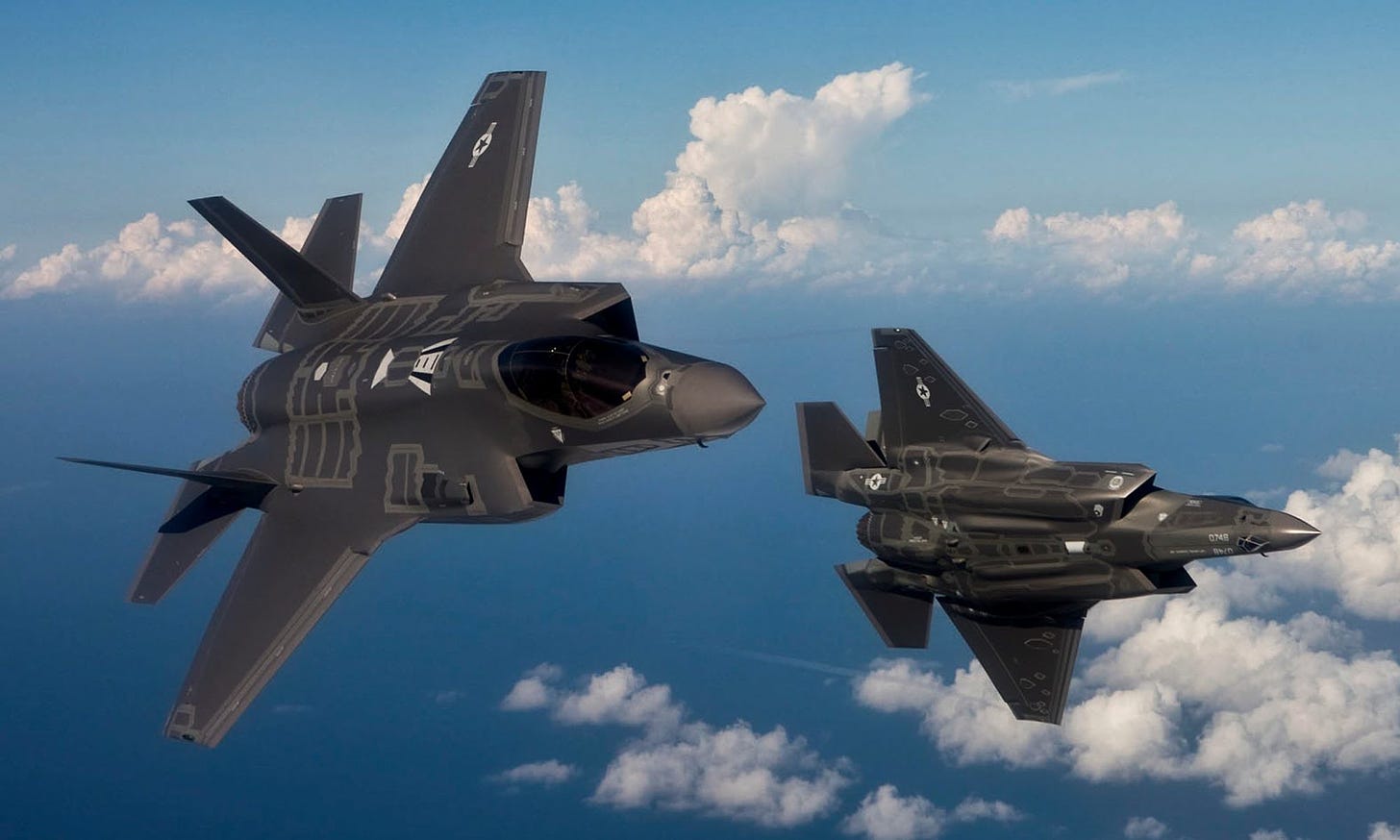 Two F 35 figher jets roll away from each other in the sky