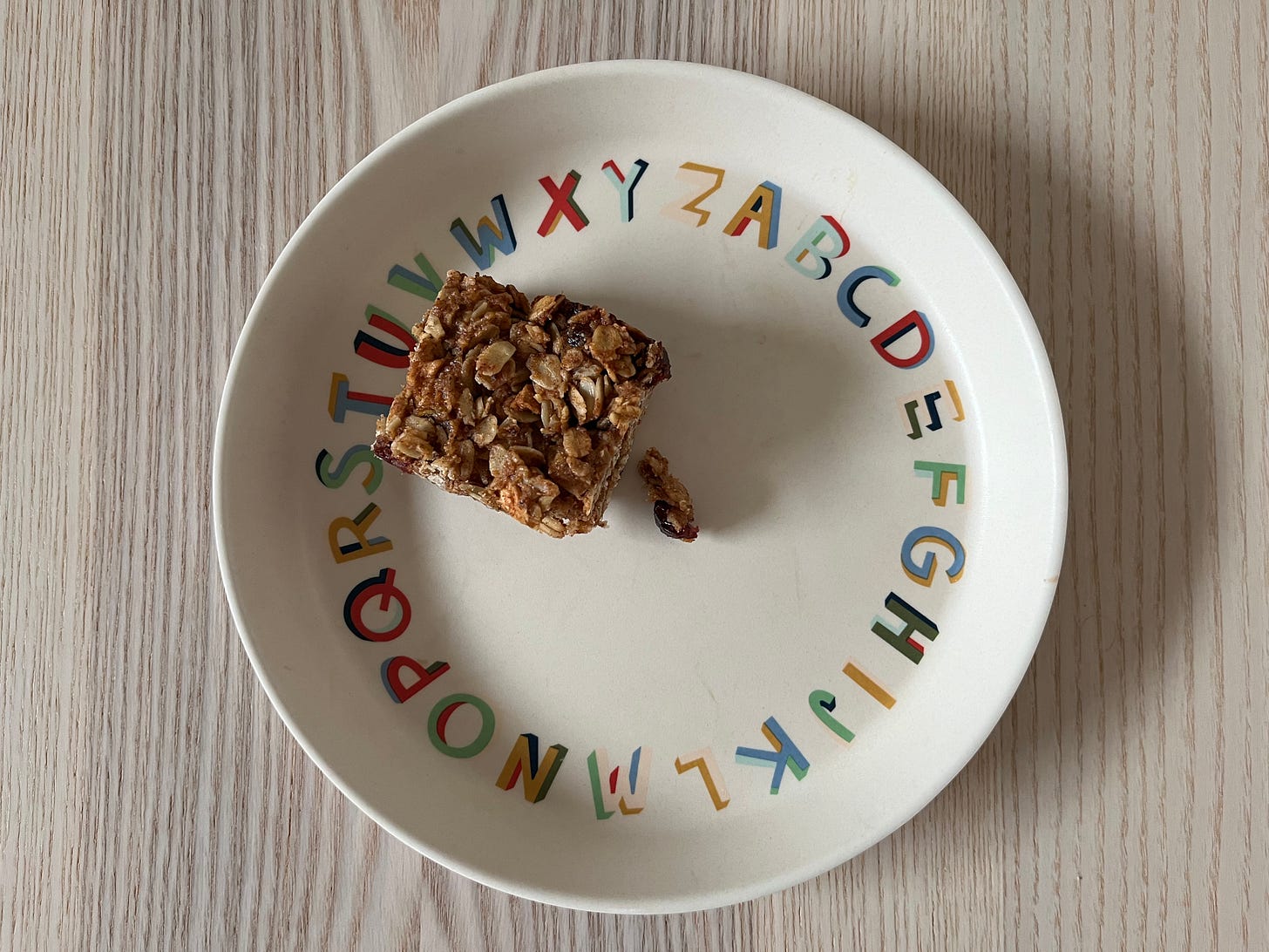 A square chewy apple-almond granola bar on a kids' plate with the alphabet on it.