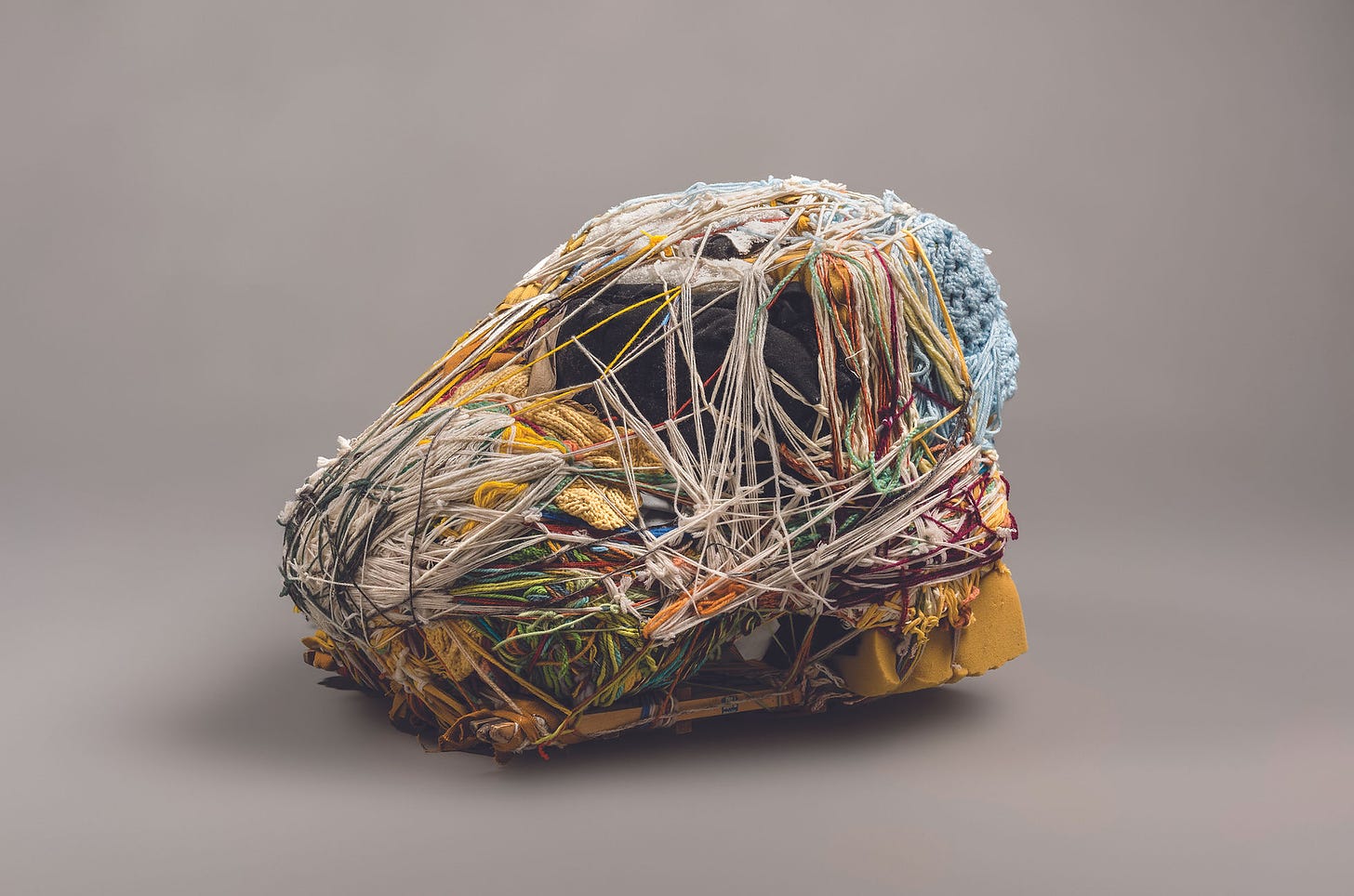 A fiber work by Judith Scott shows many threads pulled over an object of uncertain size.
