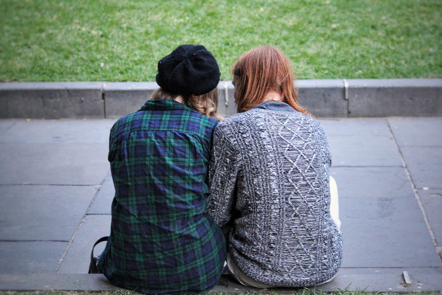 Young women leaning against each other, photographed from behind.