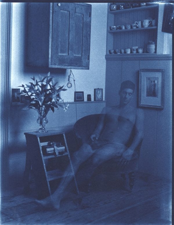 Autoportrait cyanotype de John Dugdale, assis nu dans un fauteuil les yeux fermés, un livre posé sur ses parties intimes. Son corps est transparent.