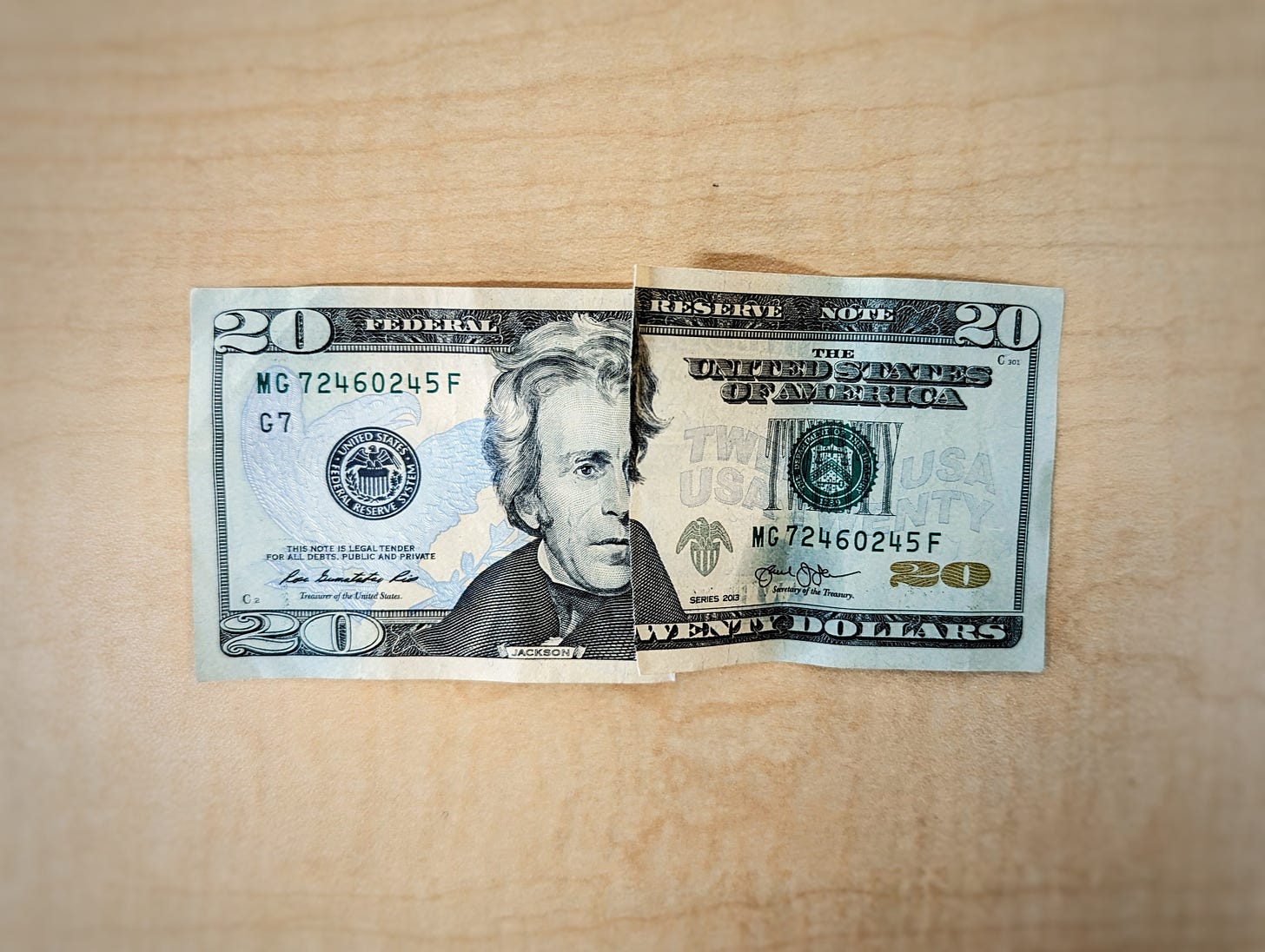 photo of a twenty dollar bill placed on a wood surface, apparently torn into two halves