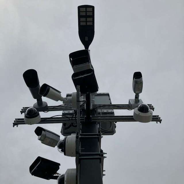 A photo of a street light with multiple cameras attached to it.