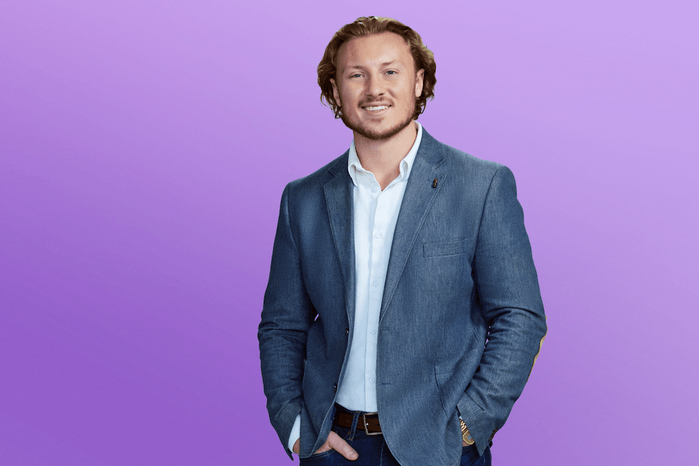Johnny wearing a blue suit with his hands in his pocket, posing in front of a purple background