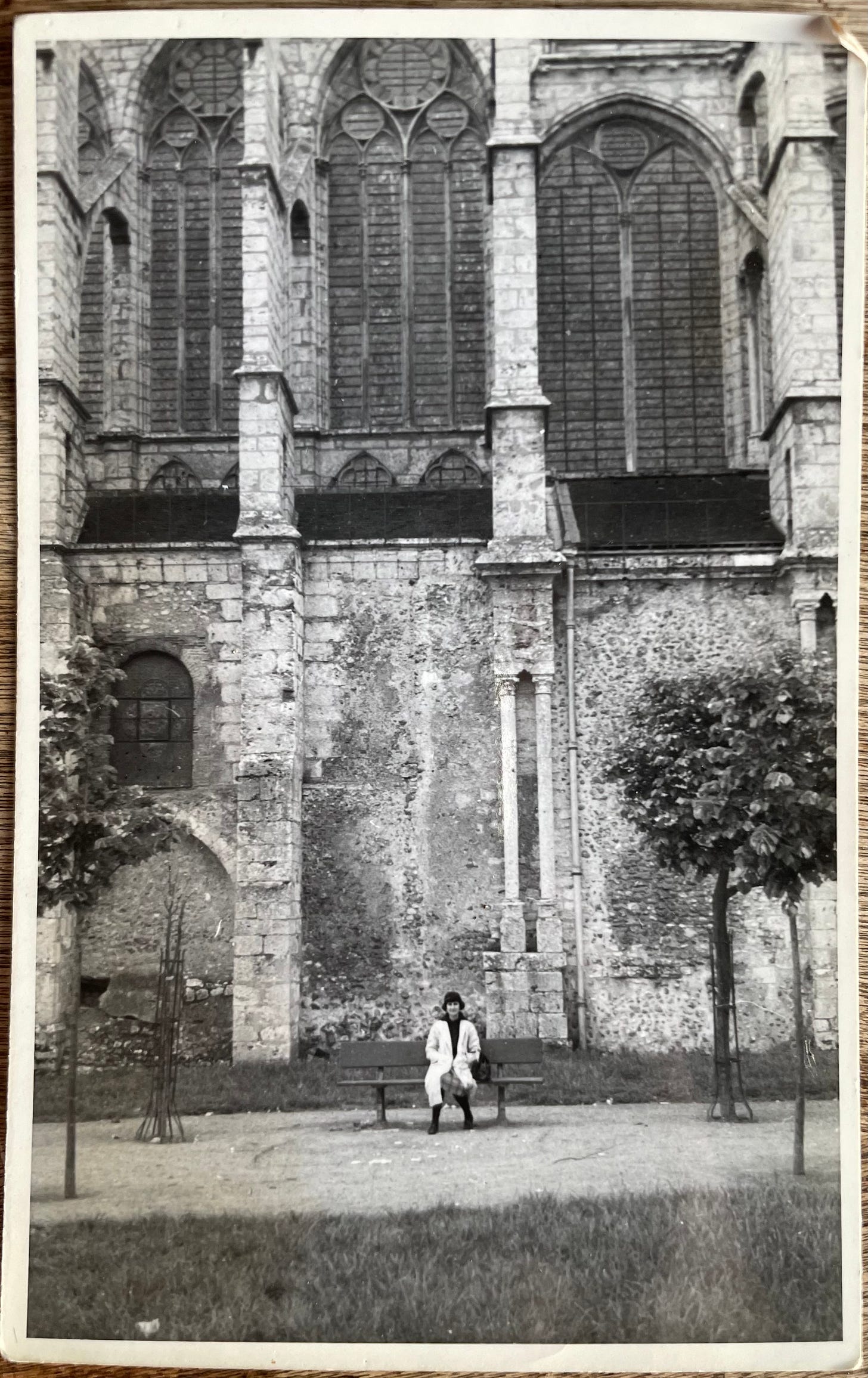 A black-and-white photo of an exterior cathedral wall with a woman seated on a bench, tiny, in the foreground.