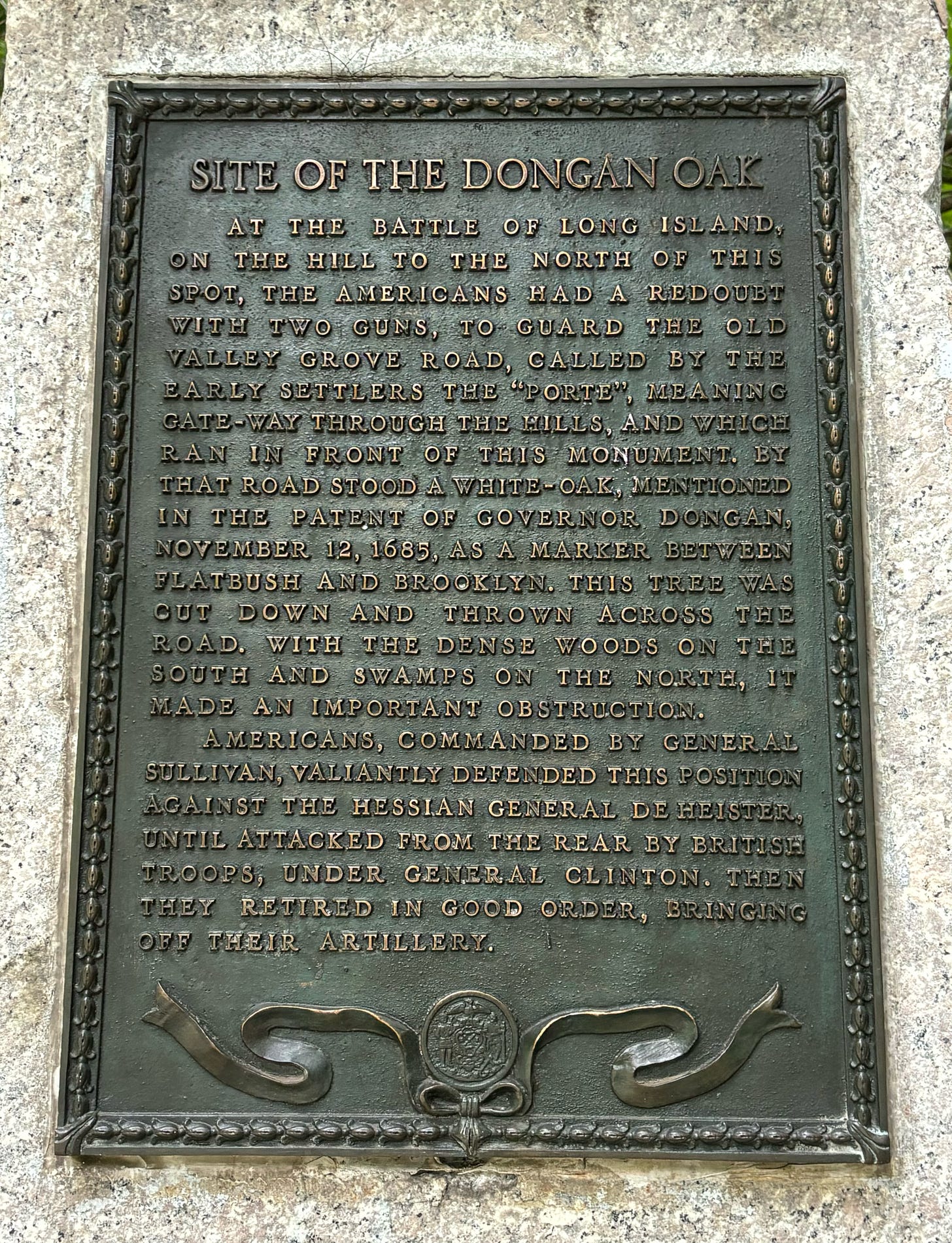 The Dongan Oak Plaque. It reads: SITE OF THE DONGAN OAK  AT THE BATTLE OF LONG ISLAND, ON THE HILL TO THE NORTH OF THIS SPOT, THE AMERICANS HAD A REDOUBT WITH TWO GUNS, TO GUARD THE OLD VALLEY GROVE ROAD, CALLED BY THE EARLY SETTLERS THE "PORTE", MEANING GATE-WAY THROUGH THE HILLS, AND WHICH RAN IN FRONT OF THIS MONUMENT. BY THAT ROAD STOOD A WHITE-OAK, MENTIONED IN THE PATENT OF GOVERNOR DONGAN,  NOVEMBER 12, 1685, AS A MARKER BETWEEN FLATBUST AND BROOKLYN. THIS TREE WAS CUT DOWN AND THROWN ACROSS THE  ROAD, WITH THE DENSE WOODS ON THE SOUTH AND SWAMPS ON THE NORTH, IT MADE AN IMPORTANT OBSTRUCTION. AMERICANS, COMMANDED BY GENERAL SULLIVAN, VALIANTLY DEFENDED THIS POSITION AGAINST THE HESSIAN GENERAL DE HEISTER, UNTIL ATTACKED FROM THE REAR BY BRITISH TROOPS, UNDER GENERAL CLINTON, THEN THEY RETIRED IN GOOD ORDER, BRINGING OFF THEIR ARTILLERY. 