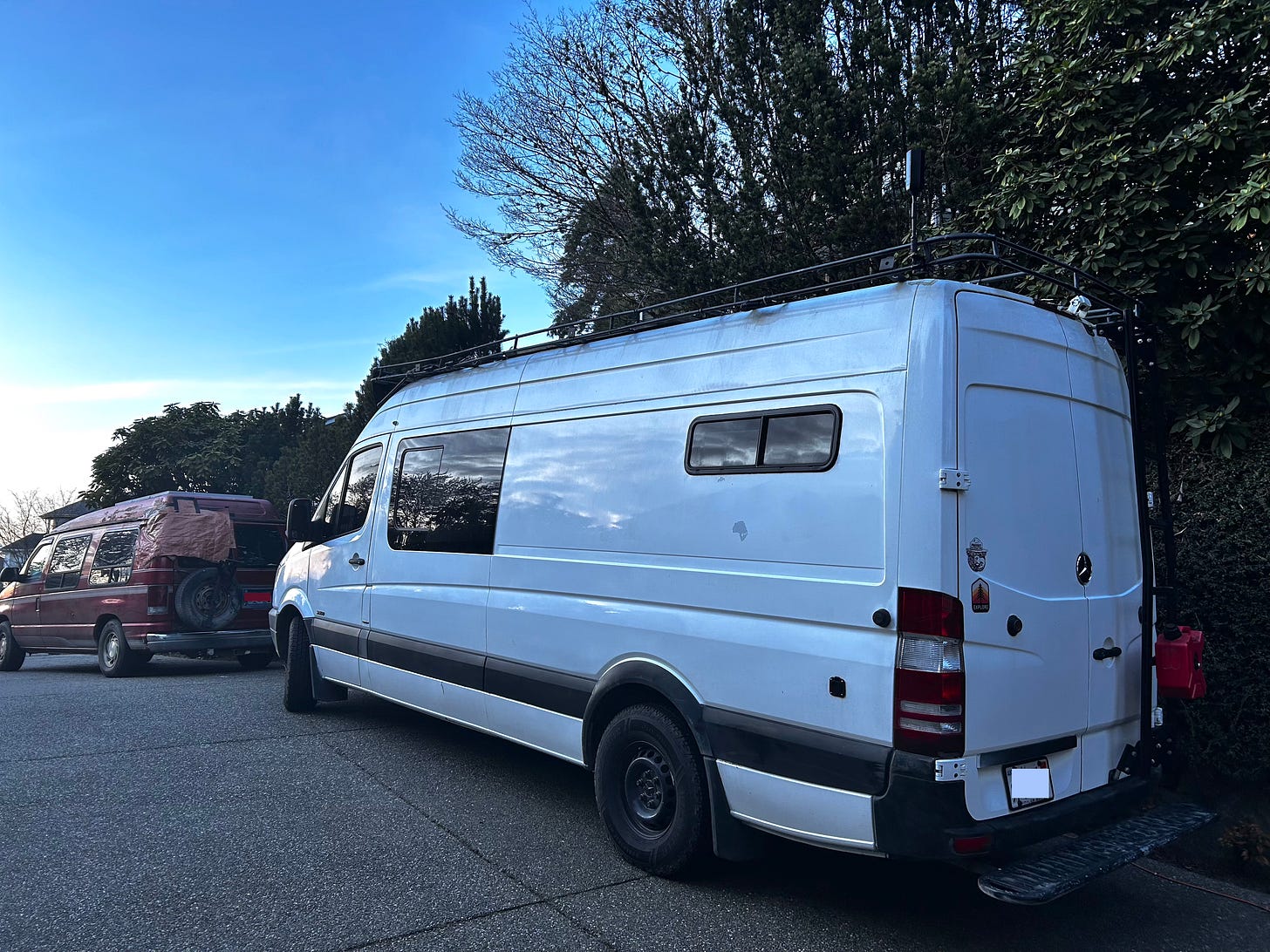 Two vans at dusk in a long driveway, a smaller ruby-colored van in front of a tall white van
