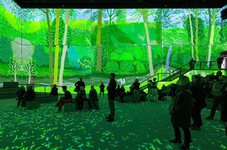 People standing in a room which has large-scale artworks projected onto the walls