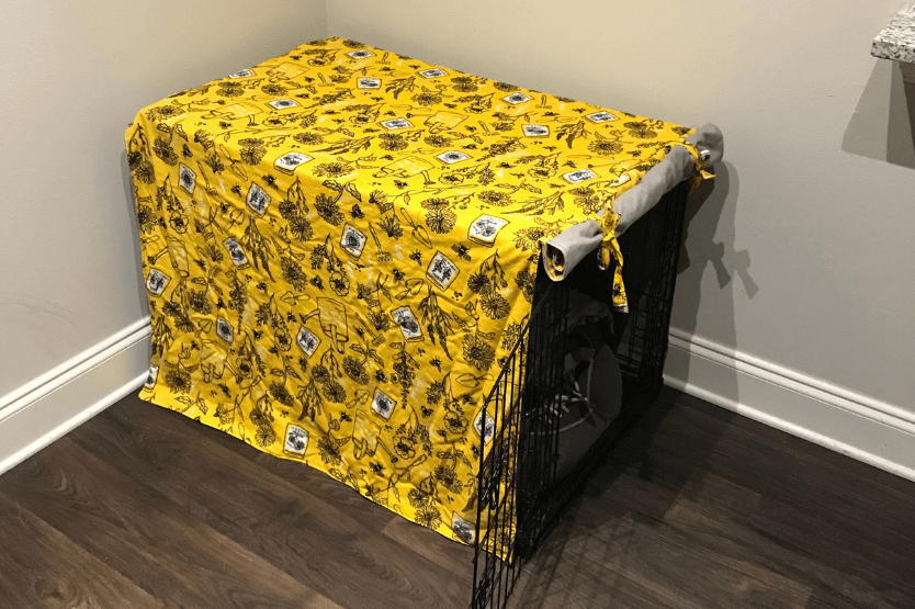 A black wire dog crate covered by a yellow floral fabric cover