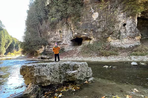 A picture of my kid, standing on a big rock in the middle of a river running through a gorge.