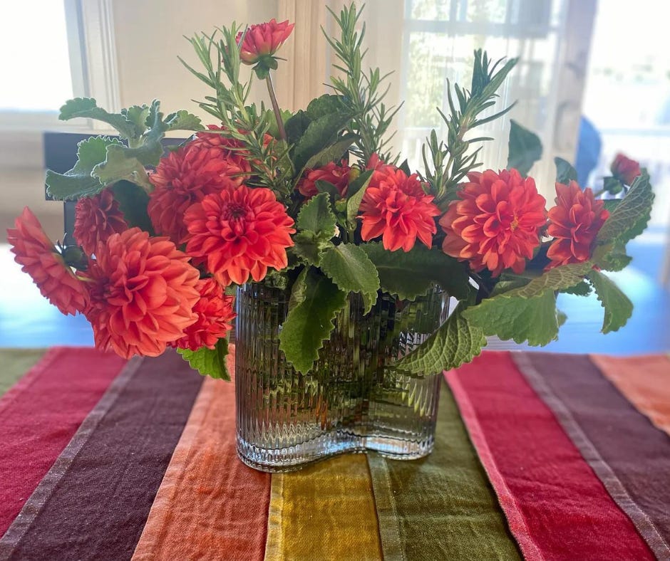 Orange dahlias in a clear curved vase on a multicolor runner