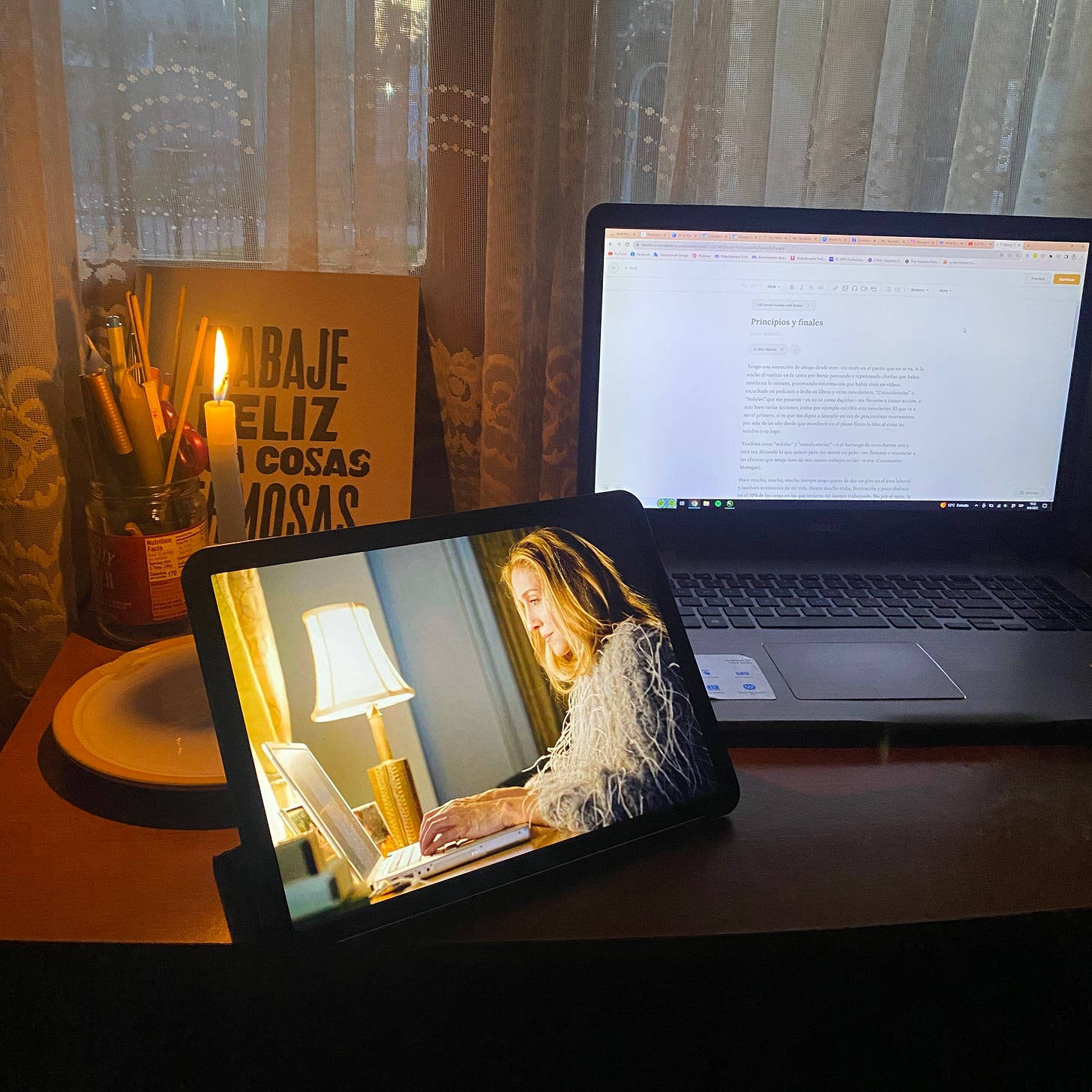 Imagen de mi escritorio con mi laptop, una vela y una imagen de Carrie Bradshaw escribiendo en su laptop