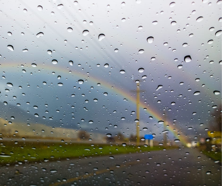 rainbow crossing the sky, as seen through a car window covered with raindrops