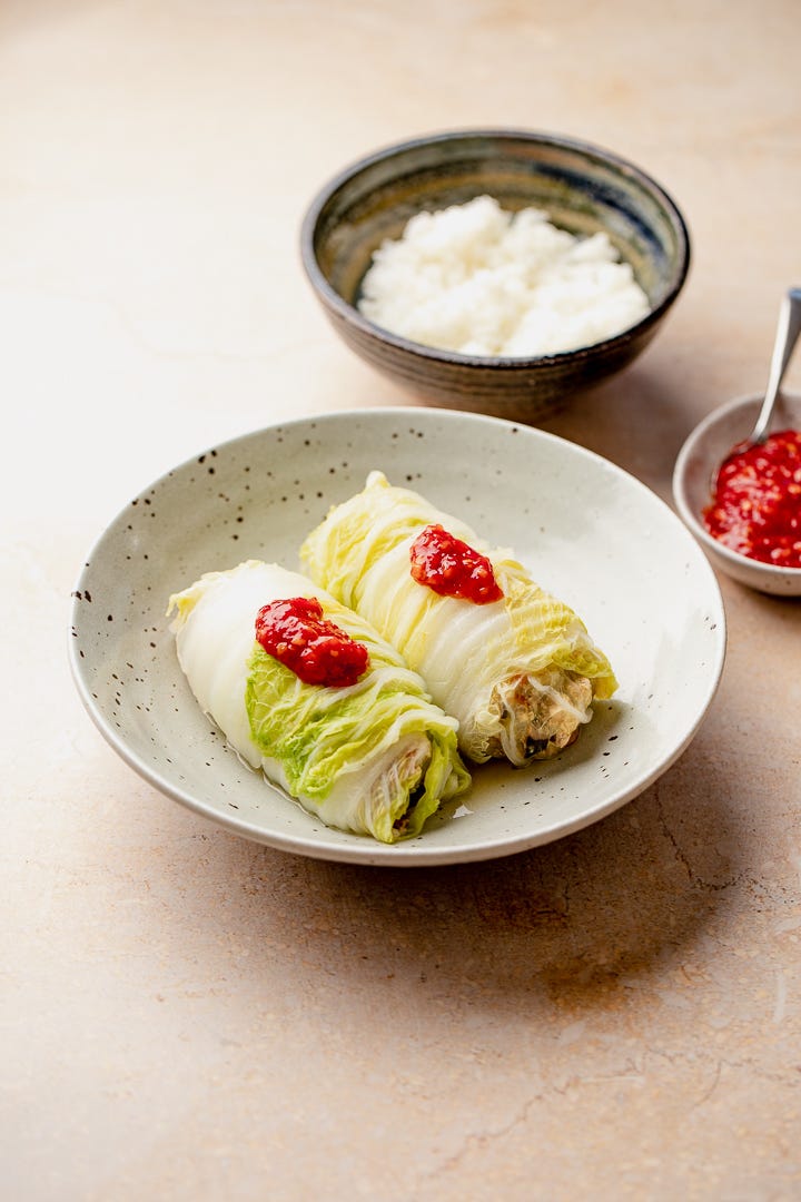 A bowl with two cabbage rolls and a dollop of chilli garlic sauce on top. 