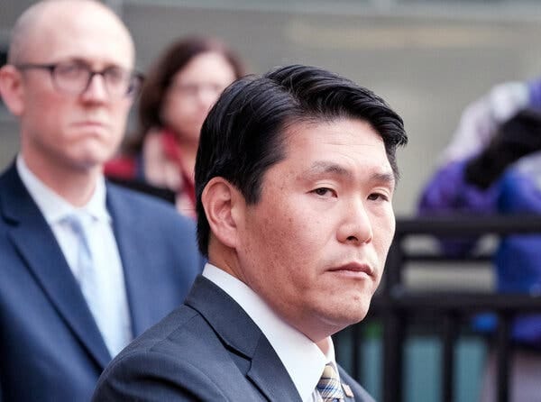 Robert K. Hur in a suit and tie at a news conference, with people standing behind him.