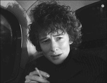 Cate Blanchette as a respresentation of Bob Dylan in a car holding a cigarette.  She has a worried expression on her face.