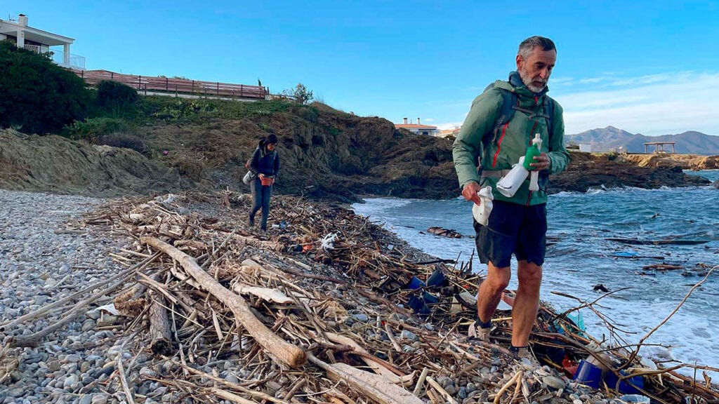 Fer, en primer plano, y Patri recogen basura en una playa llena de restos de madera