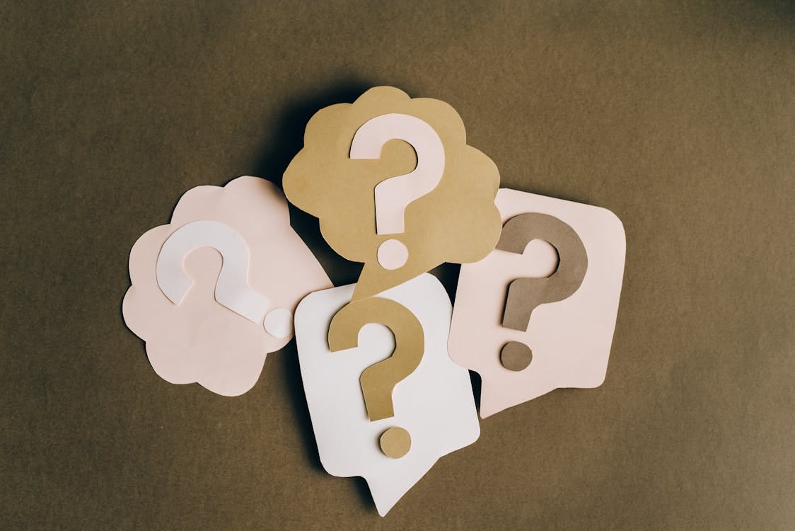 Free Four paper cutouts of question marks in beige and white on a brown surface, symbolizing inquiry and curiosity. Stock Photo