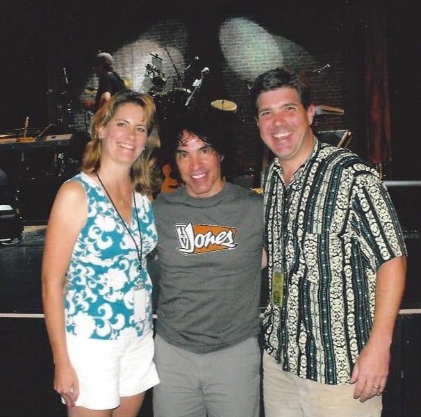 Smiling woman and man pose backstage with singer John Oates