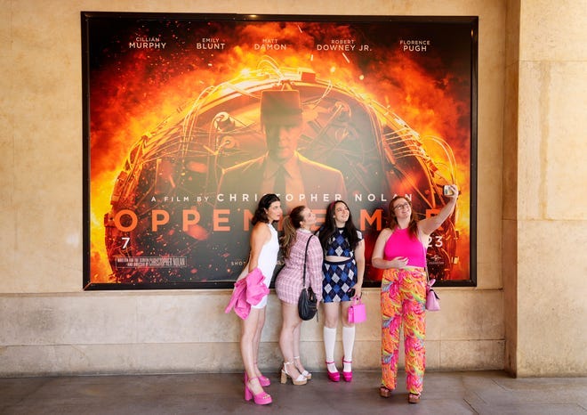 Moviegoers take a selfie in front of an "Oppenheimer" movie poster before they attended an advance screening of "Barbie."