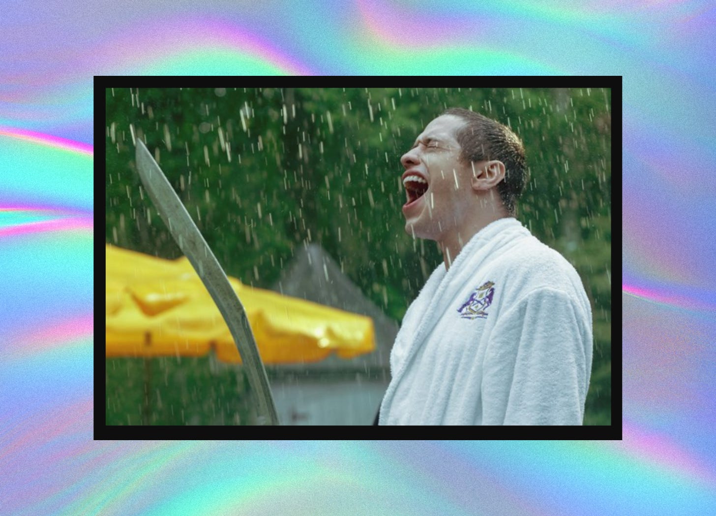 A screenshot of Pete Davidson holding a katana and yelling in the rain. His eyes are closed and he’s wearing a white bathrobe. The screenshot is cropped in the center of the frame. Behind it is a groovy purple and blue swirling background.