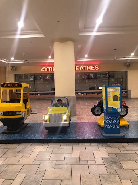 Three coin operated mechanical rides shaped like vehicles in front of a disused box office.