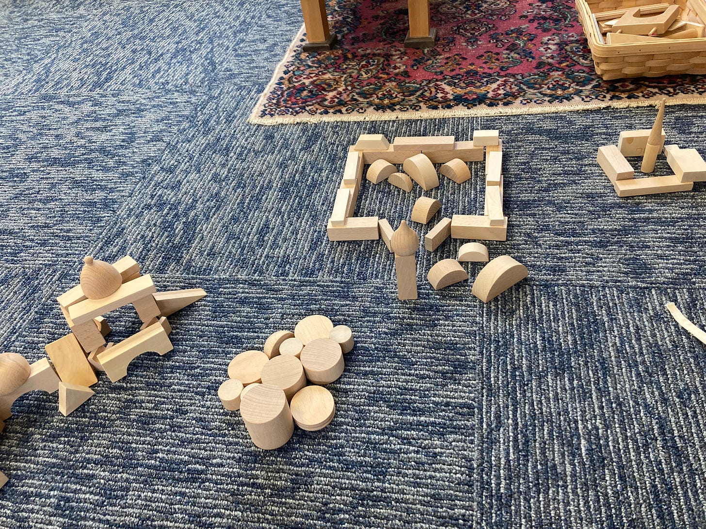 a variety of clusters of light wood building blocks are set out on blue carpet