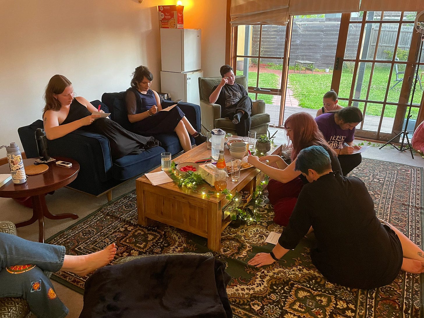 A group of eight people sitting in a living room, each writing on a piece of paper.