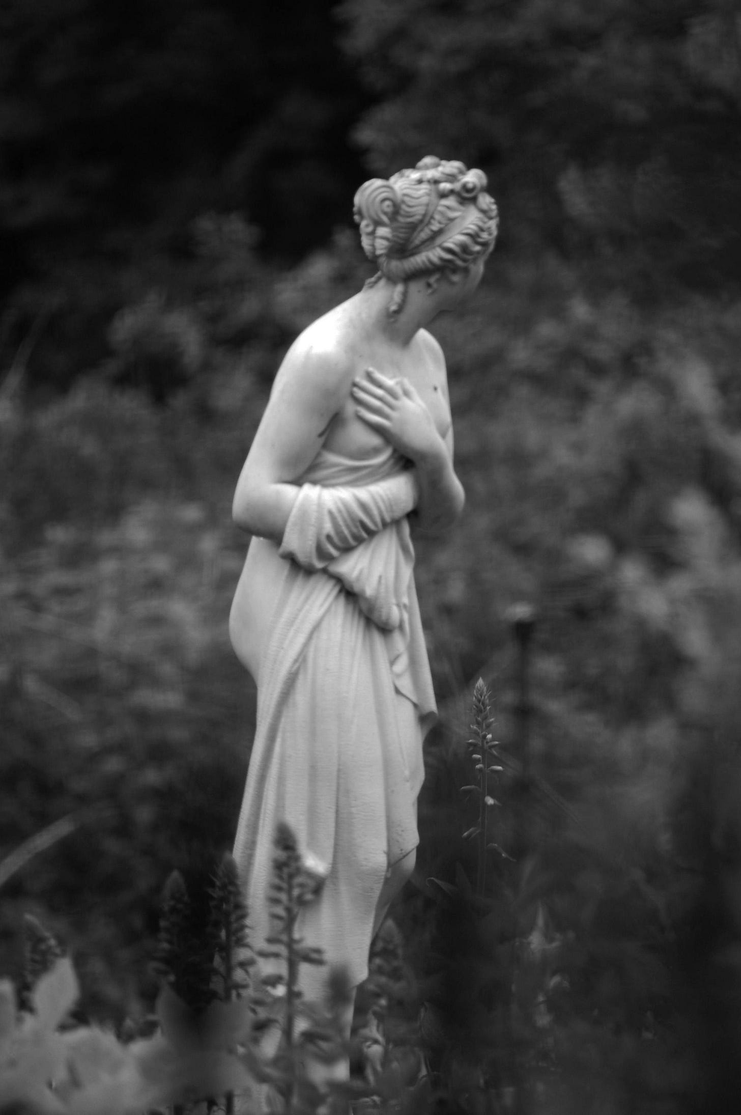 black and white pic of a statue of a woman looking away in a wild garden