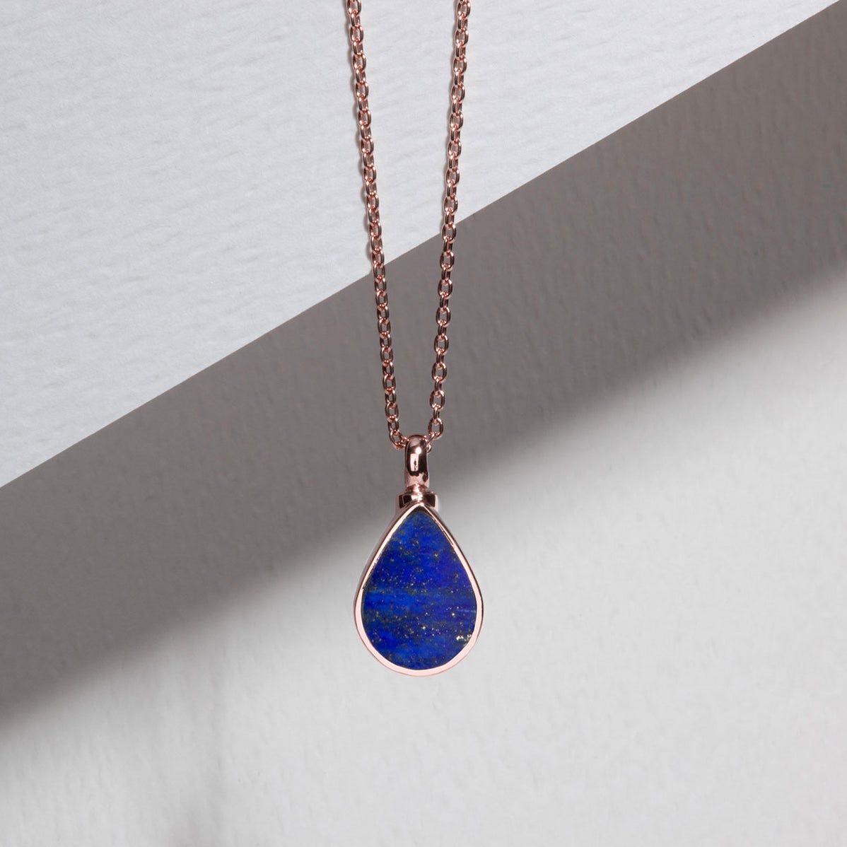 a tear-drop shaped pendant of deep blue, gold-flecked lapis lazuli, in a rose gold setting, on a rose gold chain