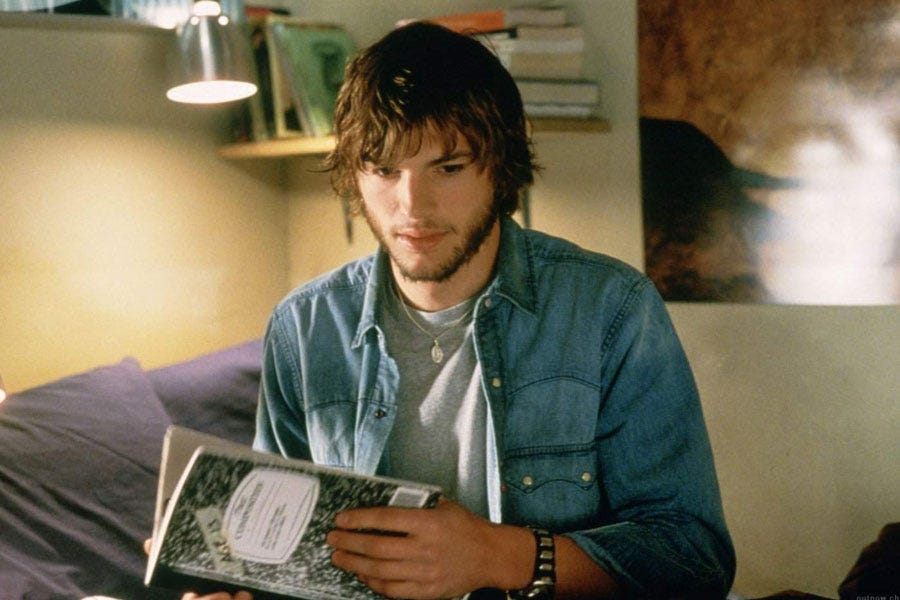 Movie still from The Butterfly Effect. Ashton Kutcher sits in a university dorm room, holding a journal in his hands.