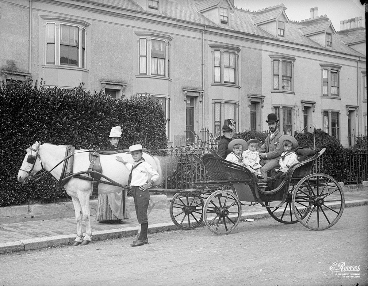 An old black and white photo featuring a family sitting in and standing around a horse and cart