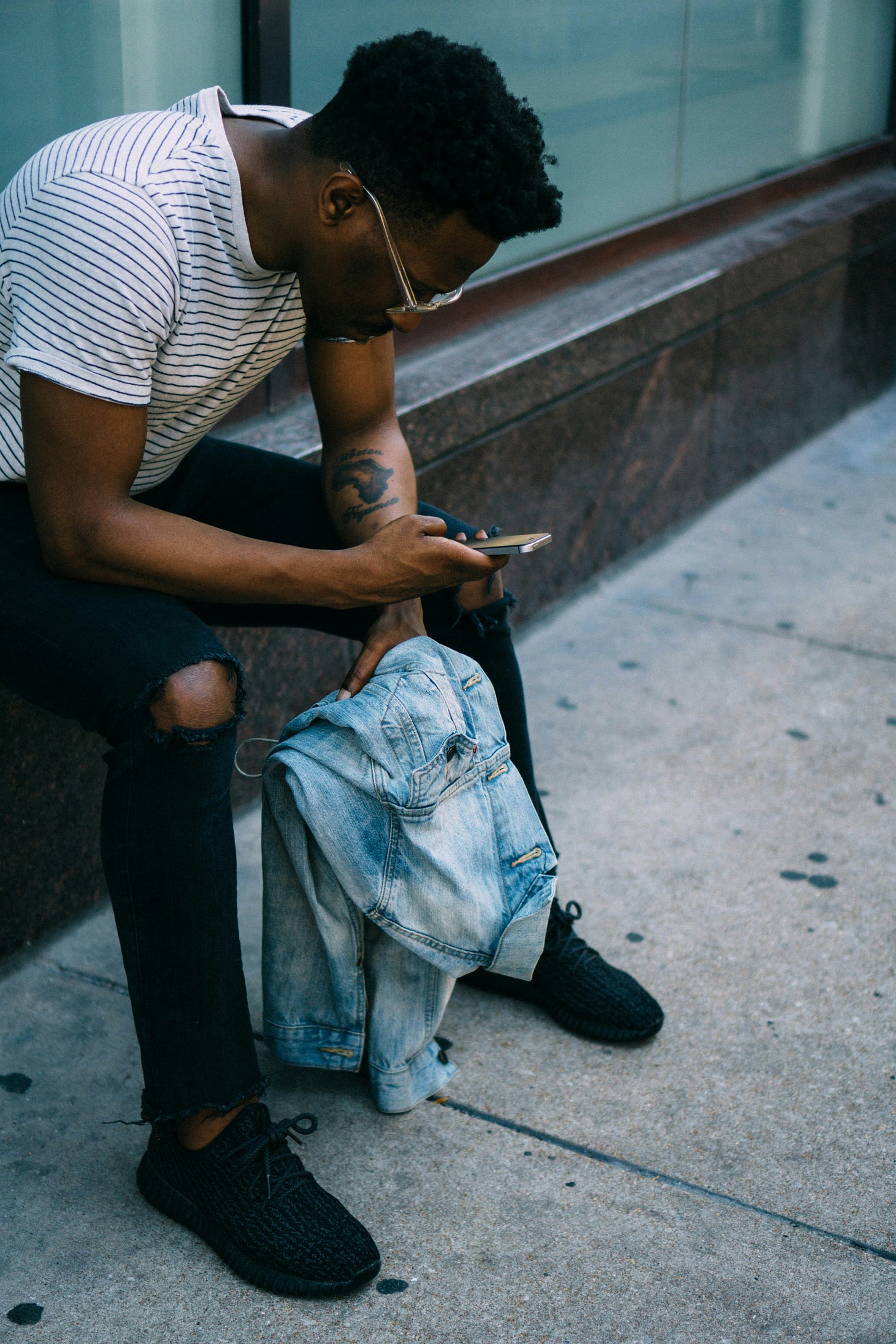 black man looking at phone while sitting on street corner