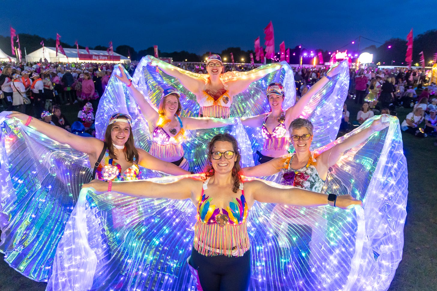 Group of women wear decorated bras and outstretch a lit-up cape