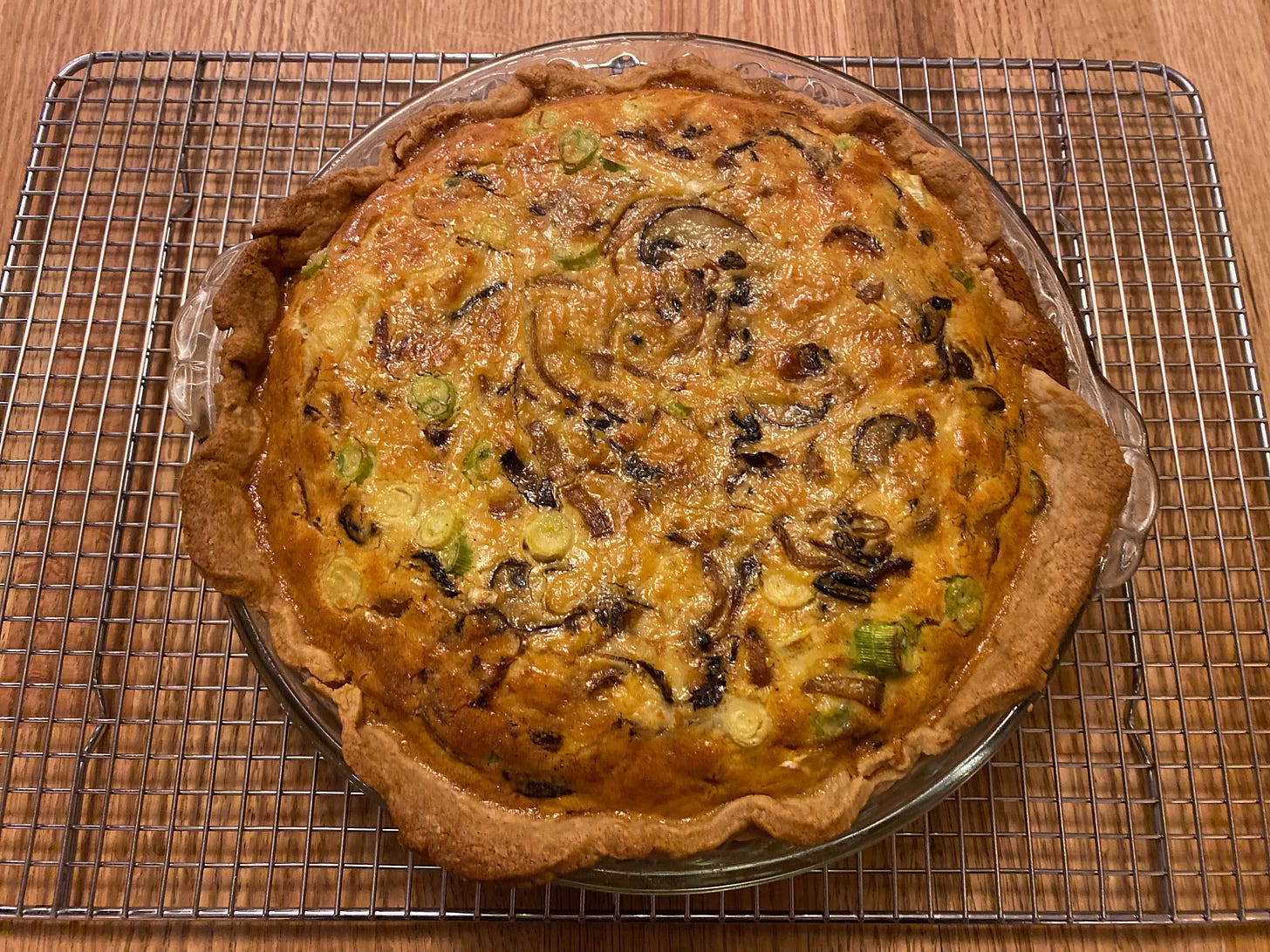 A golden brown mushroom quiche on a metal cooling rack on a kitchen counter.