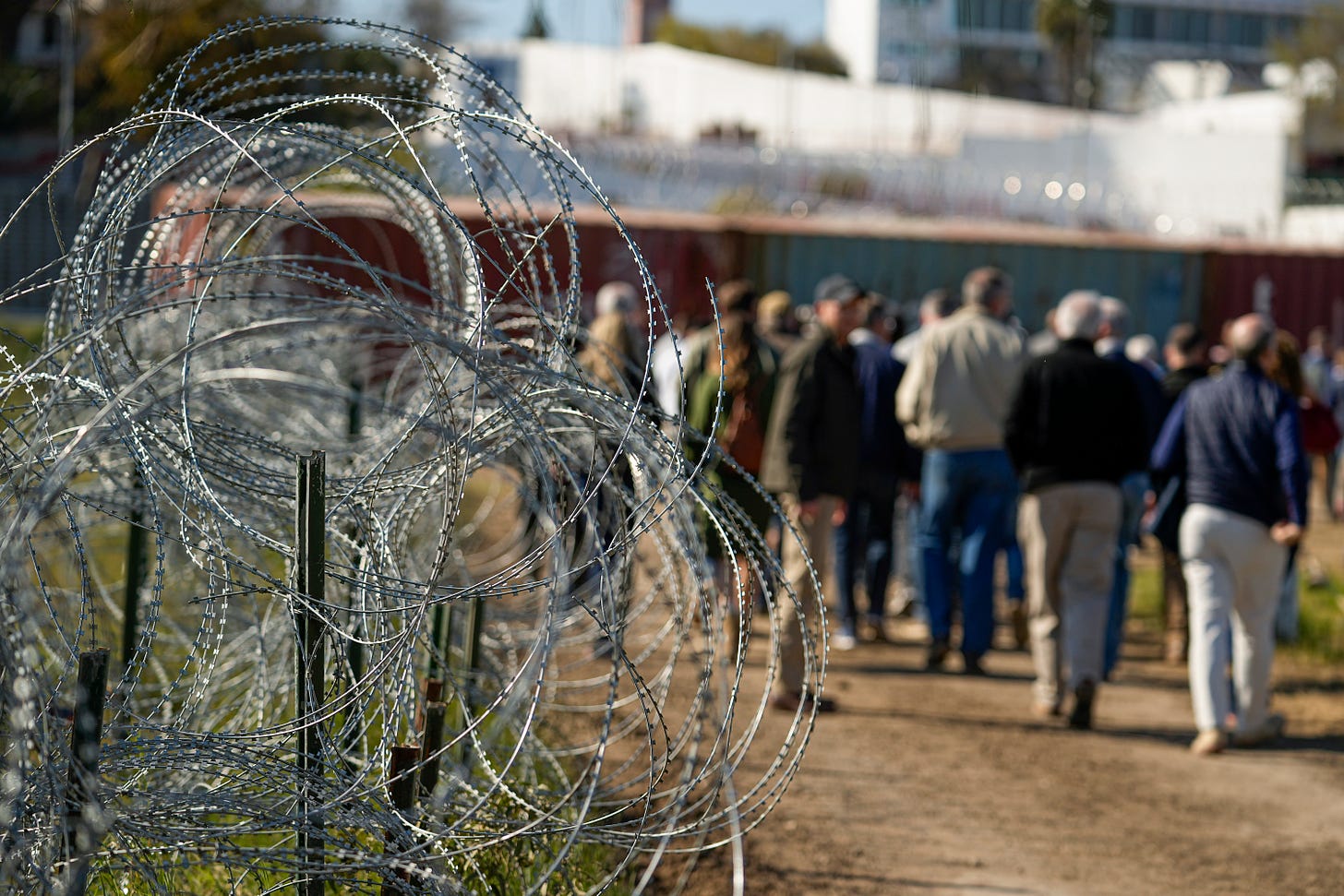 Concertina wire lines a dirt path as members of Congress walk past during a tour near the Texas-Mexico border