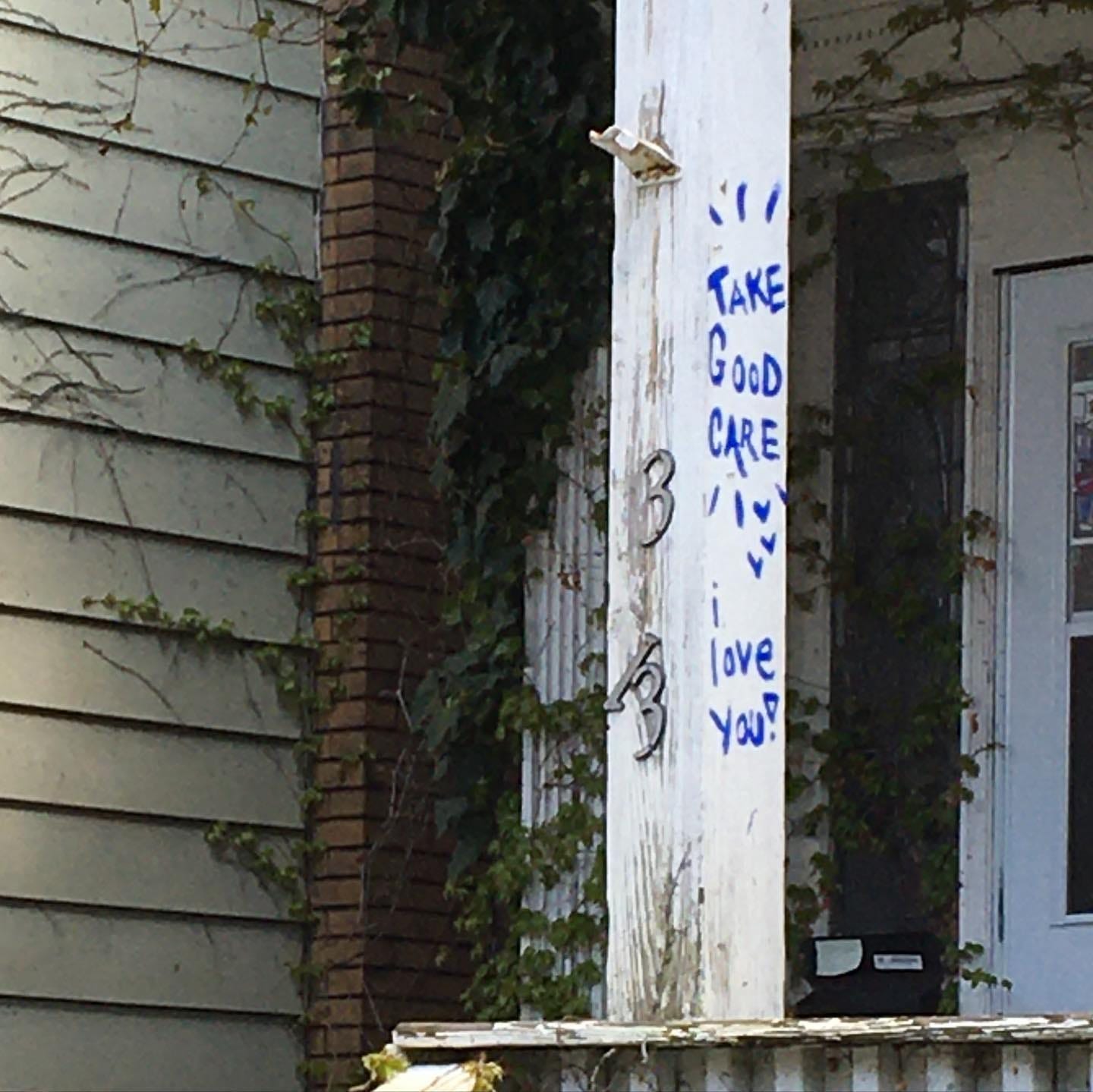 The white post on a porch has blue graffit on it that reads "Take good care! I love you!" The white post on a porch has blue graffit on it that reads "Take good care! I love you!"