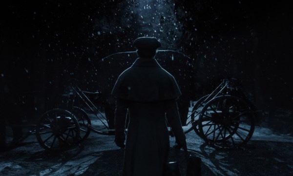 A man wearing a coat and hat walks away from the camera toward a carriage on a snowy night