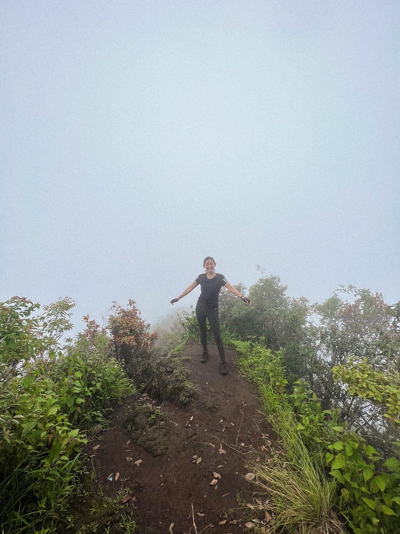 Girl smiling on top of a foggy mountain, surrounded by plants