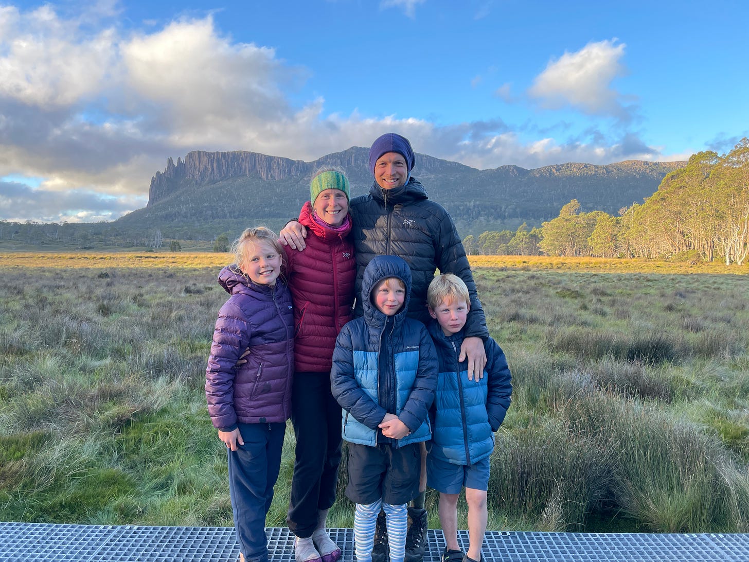 family portrait outside with sunset on the mountains, 2 adults and 3 kids wearing down jackets