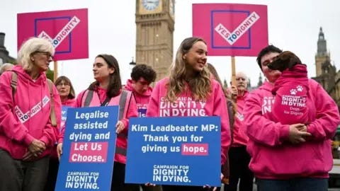 Getty Images A group of campaigners in favour of legalising assisted dying are dressed in pink hoodies which say "campaign for dignity in dying", and hold placards which read "yes to dignity" at a rally outside the Houses of Parliament.