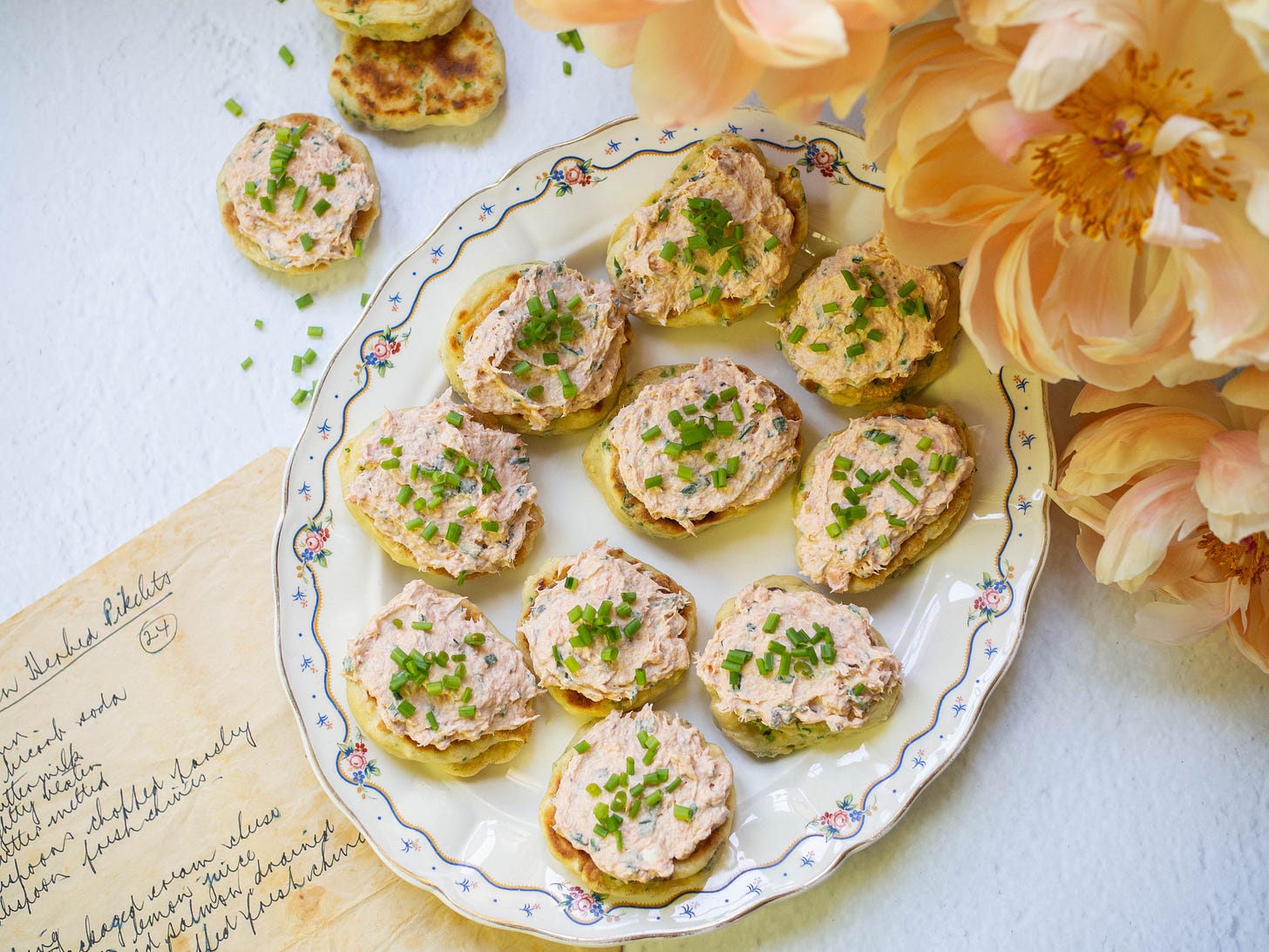 pikelets with salmon topping sprinkles with chives on an oval platter