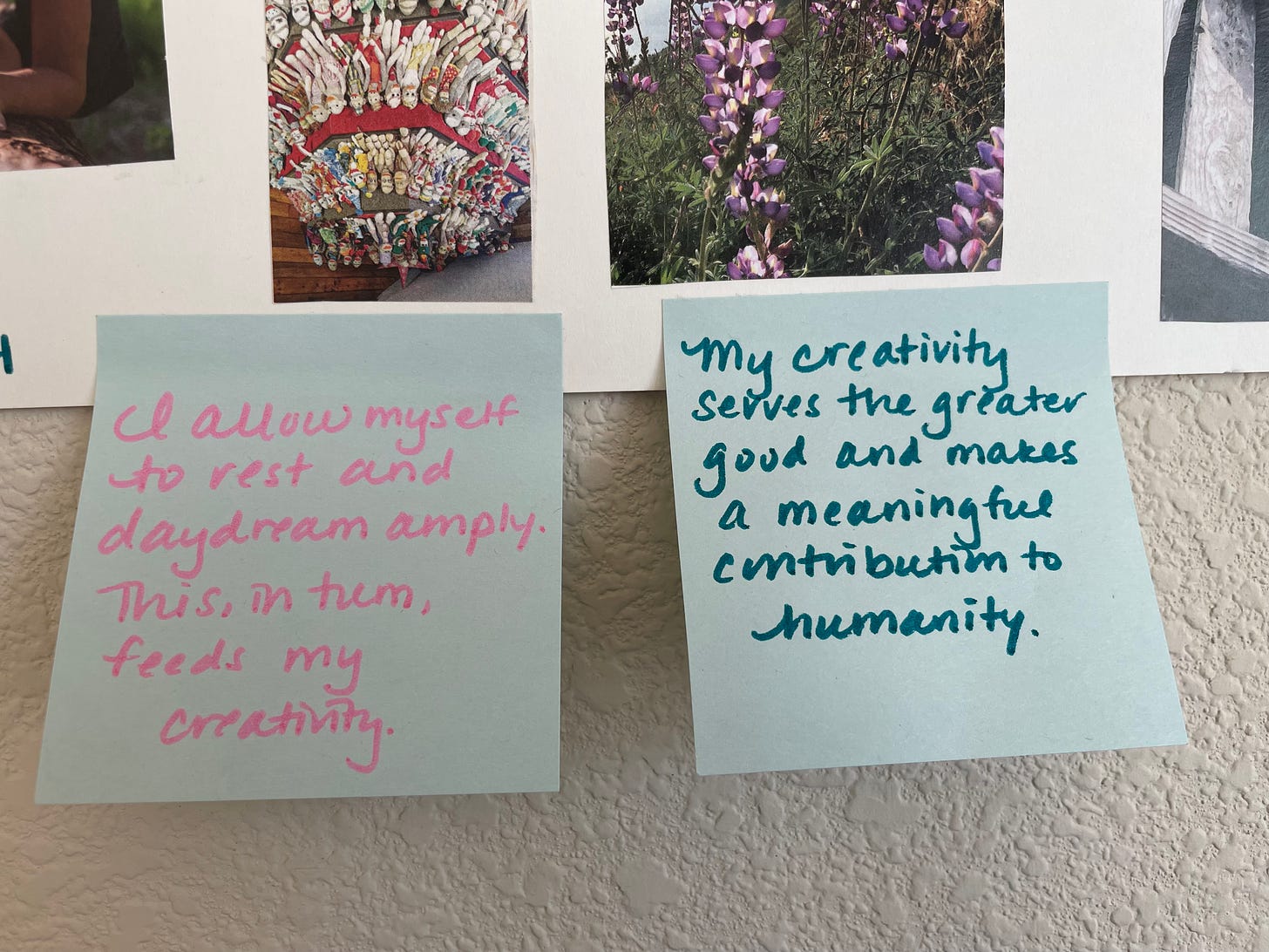 Two blue sticky notes attached to a white poster. The one on the left, written in pink marker, says: “I allow myself to rest and daydream amply. This, in turn, feeds my creativity.” The one on the right, written in blue marker, says: “My creativity serves the greater good and makes a meaningful contribution to humanity."