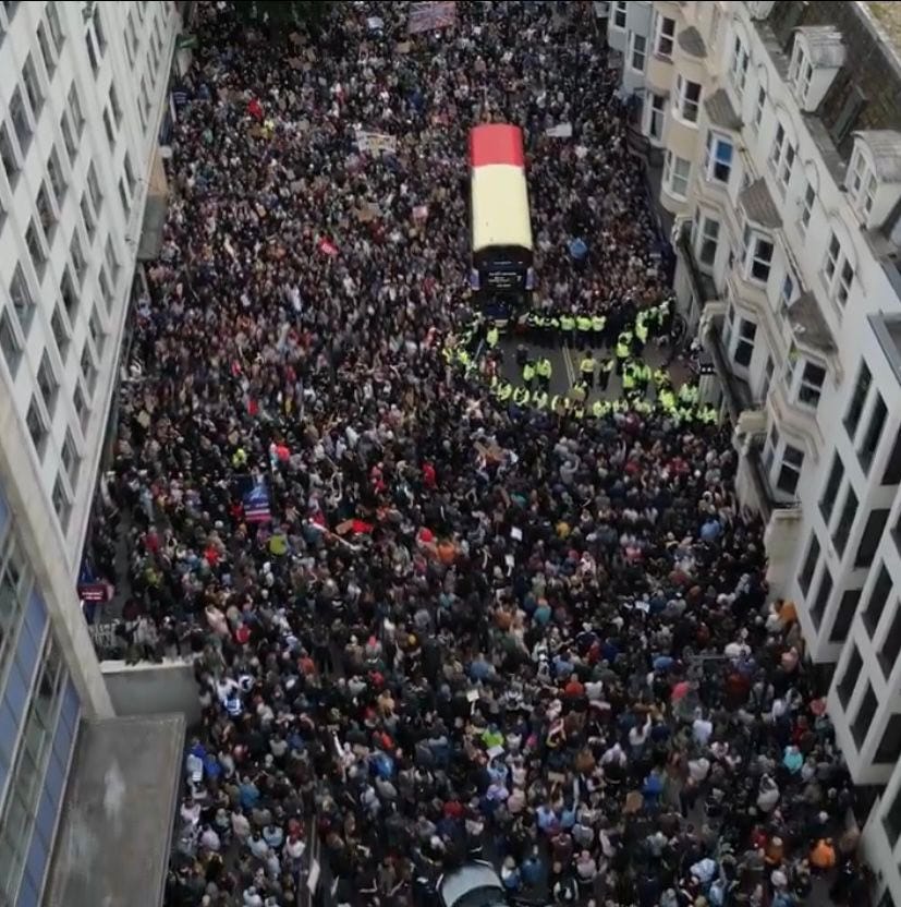 Aerial view of a street in Brighton, absolutely rammed with anti-fascist protesters.
Tiny group of 5 or 6 right wing protesters surrounded by police on the right hand side.