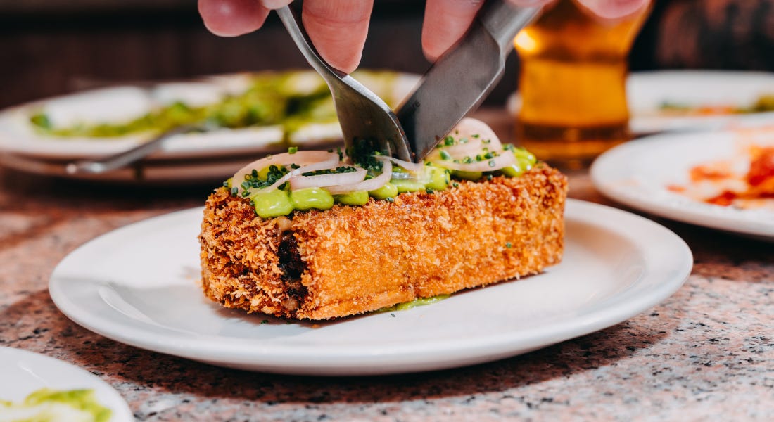 A plate with fried mushroom lasagna on it, with a silver knife and fork cutting into it