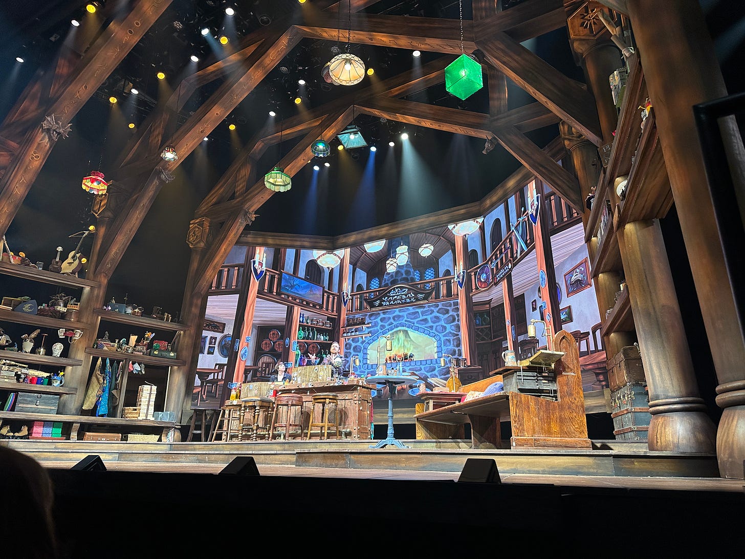 Stage for Twenty-Sided Tavern, with a screen projecting a tavernesque background, a collection of wooden benches and stools, and an assortment of random props along the far wall