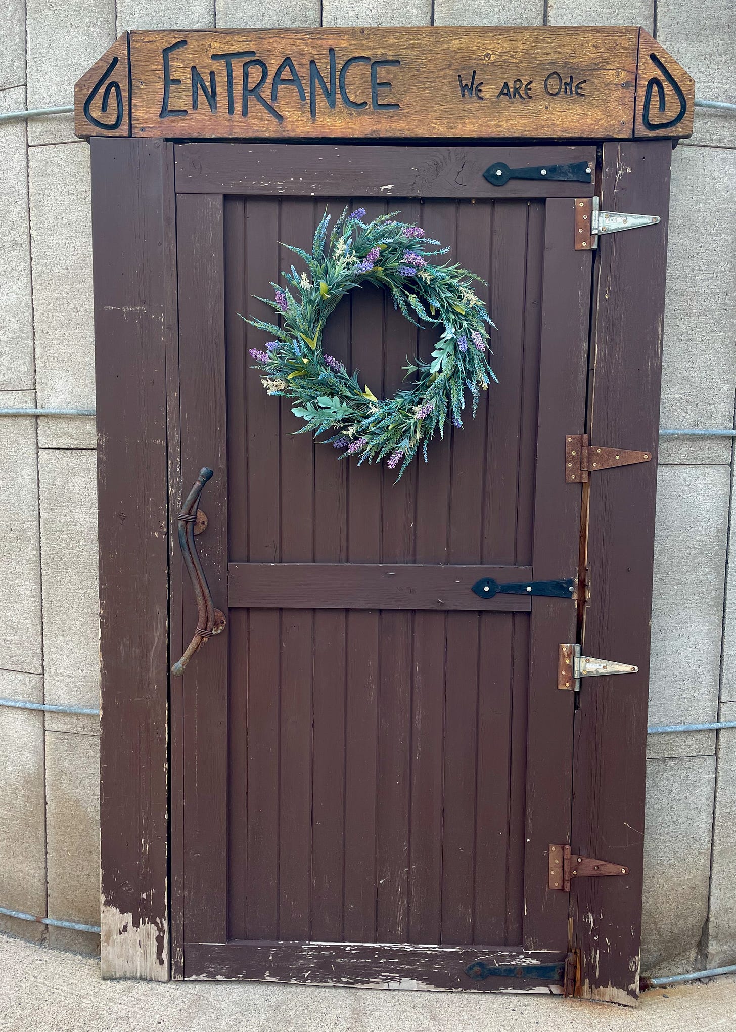 Weathered brown door with sign above reading, "ENTRANCE: We are one."